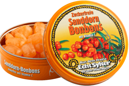 Eine orangefarbene Dose mit der Aufschrift „Sanddorn-Bonbons“ ist geöffnet. Im Inneren befinden sich ovale Orangenbonbons. Auf dem Deckel sind Sanddornbeeren abgebildet und es wird darauf hingewiesen, dass die Bonbons zuckerfrei sind und Vitamin C enthalten.
